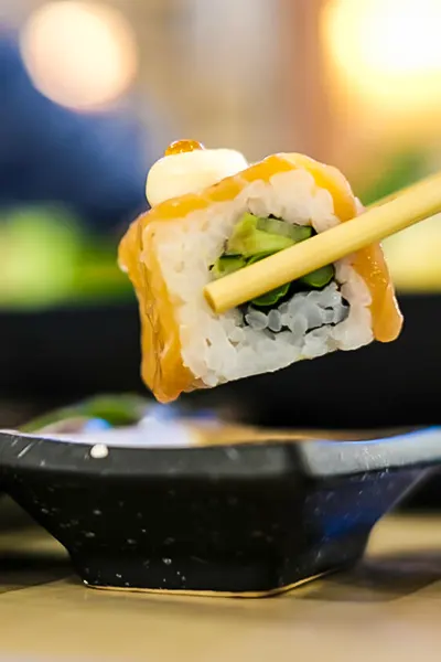 Sushi roll piece held with chopsticks, drizzled with spicy sauce and topped with a creamy finish — Casa Sensei, Fort Lauderdale