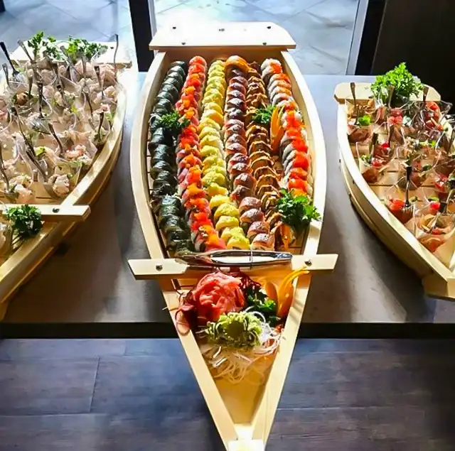Large wooden sushi boat filled with an abundant assortment of premium sushi rolls and nigiri, flanked by two smaller boats with appetizers — Casa Sensei, Fort Lauderdale